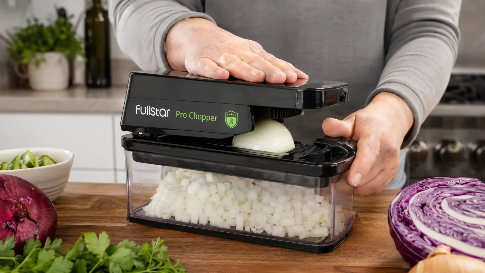 Hand pressing down on the Fullstar Pro Chopper to dice an onion into a clear container