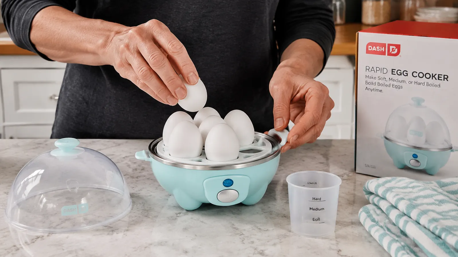 Hand placing eggs into the Dash egg cooker tray with the measuring cup nearby