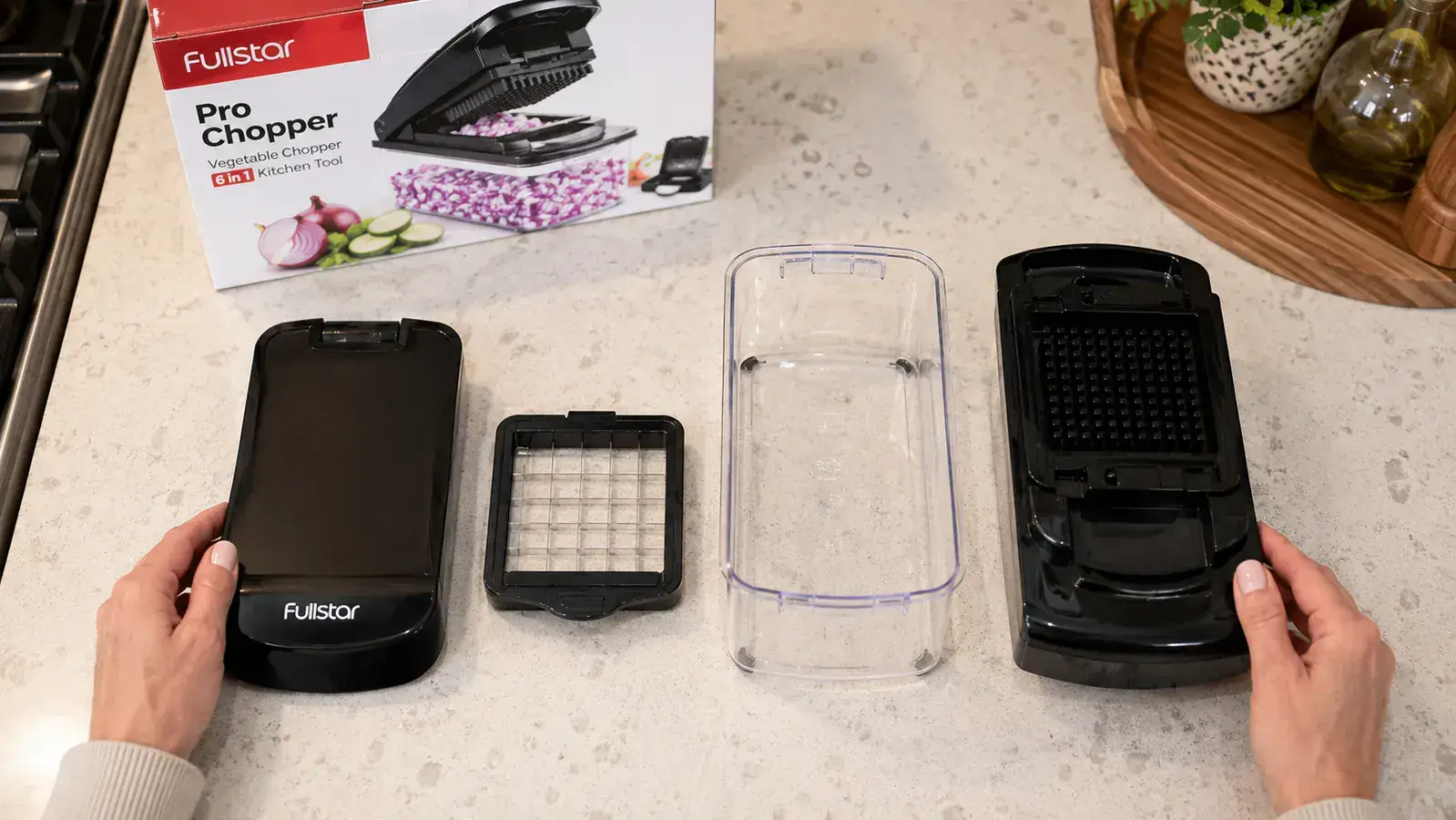 The Fullstar chopper disassembled into four parts laid flat on a countertop showing blade insert, lid, container, and base