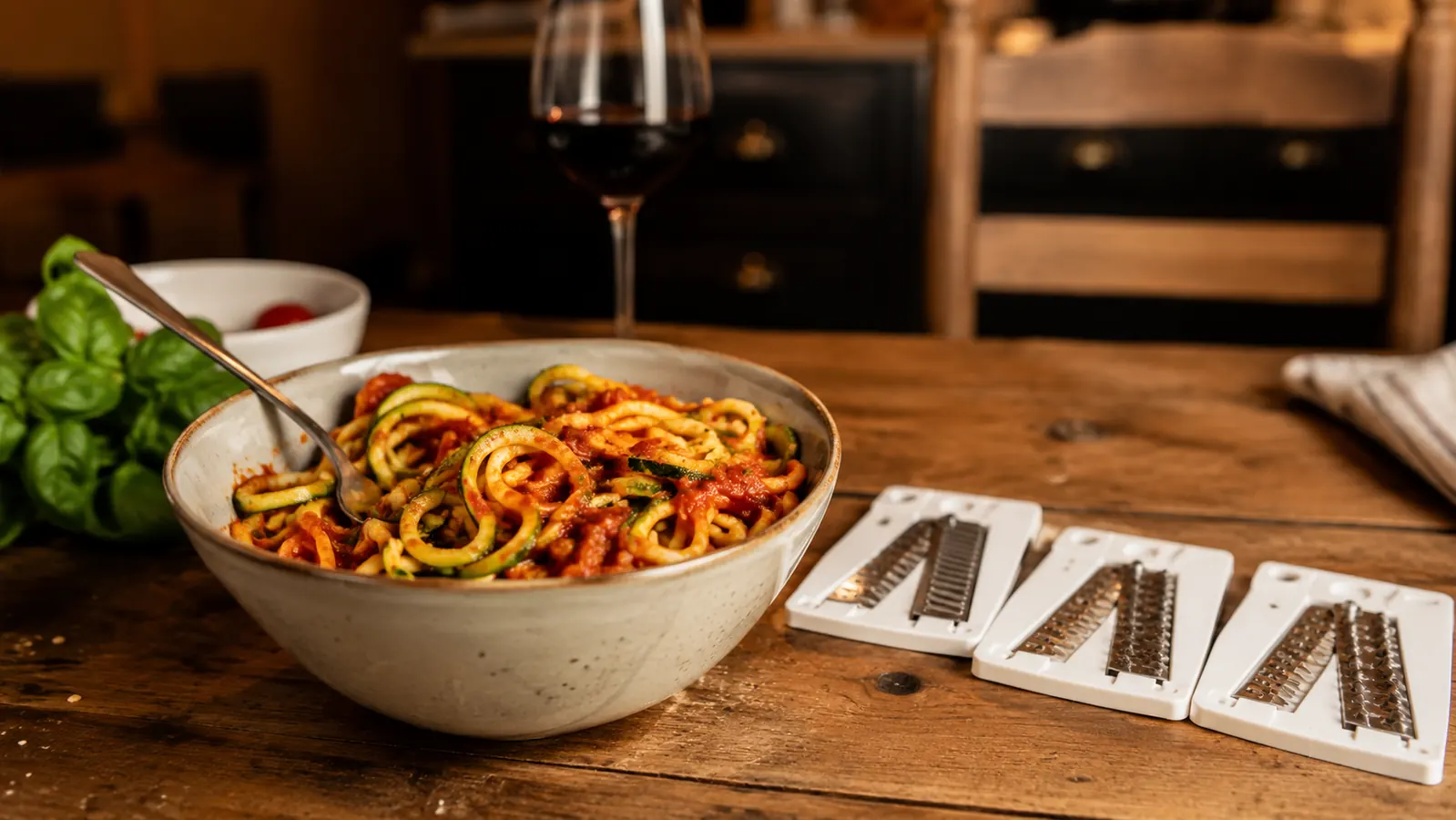 Bowl of zucchini noodles with marinara sauce on a wooden table, spiralizer blades nearby